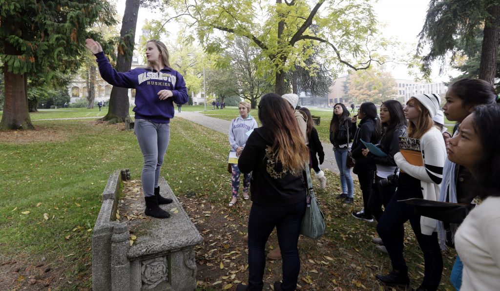 In this photo taken Tuesday, Oct. 15, 2013, University of Washington sophomore Megan Herndon, of Kailua, Hawaii, stands on a bench as she leads high school students on a tour of the campus in Seattle. Despite a downward demographic shift in the number of kids graduating from high school, enrollment is up at three of Washingtonís six public universities this fall. The University of Washington, Western Washington University and Eastern Washington University are all reporting increases in students. UW and Western also have their largest freshman classes ever. Washington State University, Central Washington University and the Evergreen State College are reporting small decreases in fall enrollment. (AP Photo/Elaine Thompson) ORG XMIT: WAET202